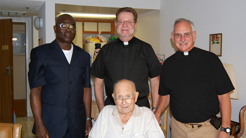 Indoor photo of two priests, a nurse, and a senior patient